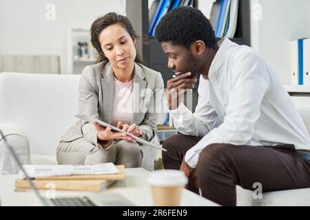 Ernsthafte, durchdachte, multiethnische Geschäftspartner diskutieren Vertragsbedingungen und lesen Vereinbarungen aufmerksam in modernen Büros Stockfoto