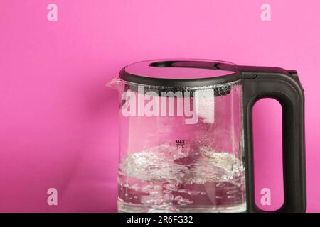 Elektrischer Wasserkocher aus Glas mit kochendem Wasser auf Rosa. Draufsicht. Stockfoto