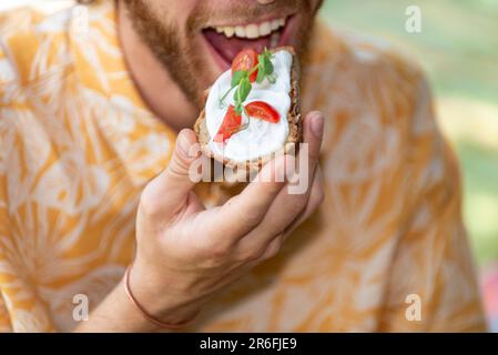 Hungriger Mann, der vegane Vorspeise in der Hand hält, bereit zum Bissen Stockfoto