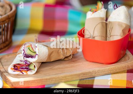 Ein paar vegane Burritos auf einem Holzteller bei einem Picknick Stockfoto