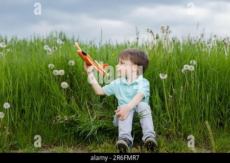 Ein Kind träumt davon, Pilot zu werden und spielt mit einem orangefarbenen Flugzeug Stockfoto