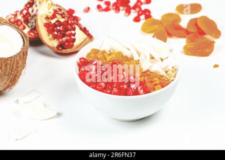 Eine weiße Oberfläche mit einer Schüssel gefüllt mit einer Auswahl an bunten Früchten, darunter Orangen, Äpfel und Bananen Stockfoto