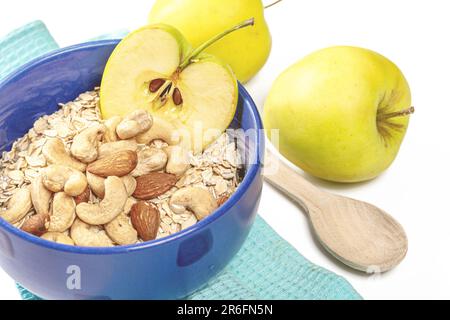 Eine weiße Keramikschüssel gefüllt mit einer Vielzahl frisch gepflückter Äpfel und Nüsse steht auf einem Holztisch Stockfoto