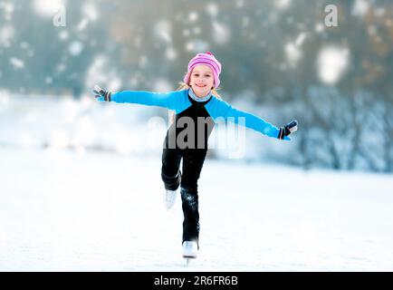 Fröhliches, süßes Mädchen in Thermalanzügen, Schlittschuhlaufen Stockfoto