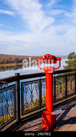 Öffentliche stationäre Ferngläser am Flussufer im Sommer oder Herbst, um die Natur zu erkunden, münzbetriebene rote Ferngläser aus Metall. Stockfoto