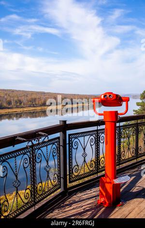 Öffentliche stationäre Ferngläser am Flussufer im Sommer oder Herbst, um die Natur zu erkunden, münzbetriebene rote Ferngläser aus Metall. Stockfoto