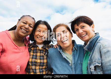 Glückliche, multiethnische Seniorinnen, die Spaß haben, auf dem Dach des Hauses in die Kamera zu lächeln Stockfoto