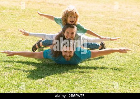 Familie liegt auf Gras im Park. Fly-Konzept, kleiner Junge sitzt Pickaback, während der Flug imitiert. Stockfoto