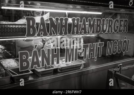 Zwei junge Frauen bereiten traditionelle vietnamesische Banh mi-Sandwiches in einer Bäckerei in Kontum im zentralen Hochland Vietnams zu. Auf dem Schild steht: Aufschnitt Stockfoto