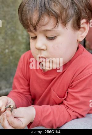 Süßer kleiner Junge, der mit Zweigen im Garten bei der Garage spielt Stockfoto