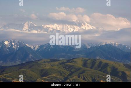 Grüne Hügel in der Nähe von verschneiten Bergen. Wunderschöne Berglandschaft im Frühling. Alatau Gebirgskette, Tien Shan in Kasachstan in der Nähe der Stadt Almaty Stockfoto