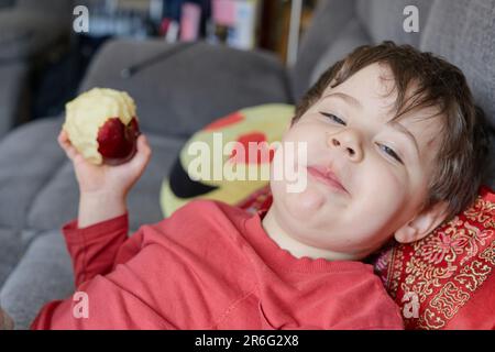 Ausdrucksstarker Junge, der einen Apfel isst und sich zu Hause auf der Couch ausruht Stockfoto