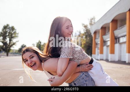 Zwei ethnische weibliche Teenager, die sich umarmen und Spaß miteinander haben. Fröhliche Freunde in lässigen Klamotten, die herumalbern und auf der Straße lachen. Süßer Junge Stockfoto