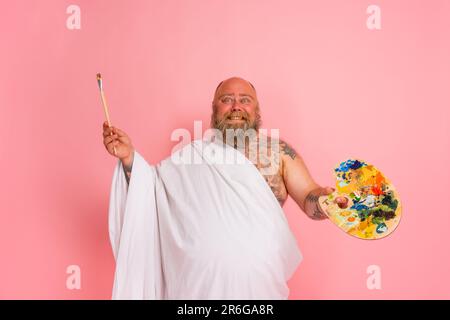 Fat man benimmt sich wie ein wichtiger Künstler mit Pinsel und Farbe in der Hand Stockfoto