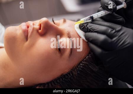 Schönheitsspritzen. Eine Kosmetikerin in transparenten Handschuhen spritzt ihrem Klienten in den Unterkiefer. Behandlung mit Hyaluronsäure. Einleitung Stockfoto