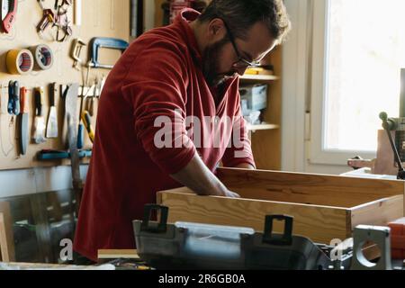 Schreiner, der ein Möbelstück in seinem kleinen Unternehmen zusammenstellt. Handwerker, die mit Werkzeugen arbeiten Stockfoto