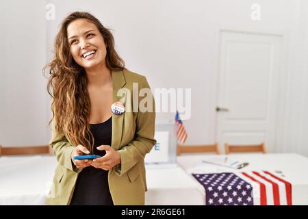 Junge schöne hispanische Frau Wahltisch Präsident mit Smartphone an Wahlhochschule Stockfoto