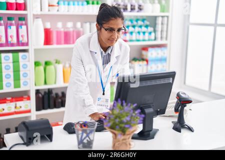 Junge schöne hispanische Frau Apothekerin mit Computer in der Apotheke Stockfoto