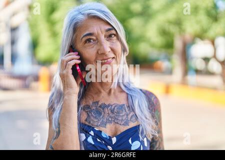 Grauhaarige Frau mittleren Alters lächelt selbstbewusst auf dem Smartphone im Park Stockfoto