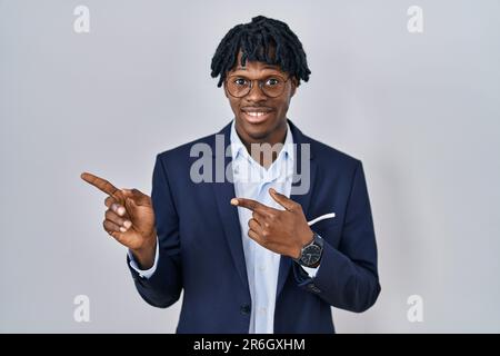 Junger afrikanischer Mann mit Dreadlocks, der eine Geschäftsjacke auf weißem Hintergrund trägt und zur Seite zeigt, besorgt und nervös mit beiden Händen, besorgt und surfend Stockfoto