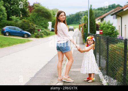 Mutter und Tochter gehen zusammen nach draußen, halten Händchen, blicken zurück über die Schulter Stockfoto