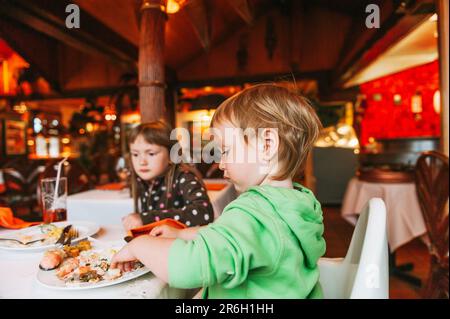 Zwei schmutzige Kinder essen im Restaurant zu Mittag, ein Kleinkind isst mit den Händen Stockfoto