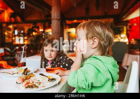 Zwei schmutzige Kinder essen im Restaurant zu Mittag, ein Kleinkind isst mit den Händen Stockfoto