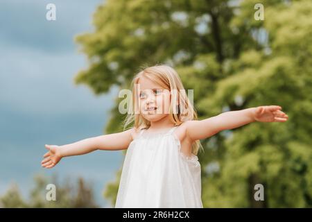 Außenporträt eines süßen kleinen Mädchens mit blonden Haaren und weit geöffneten Armen Stockfoto