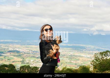 Außenporträt von einer hübschen Frau, die einen Yorkshire-Terrier-Hund hält Stockfoto