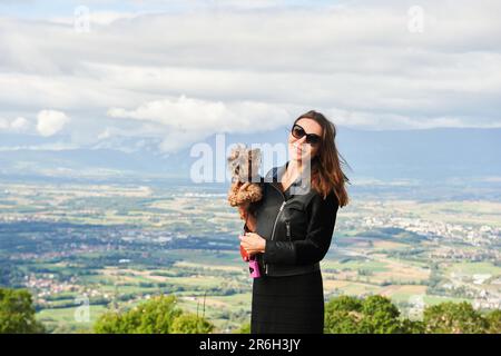 Außenporträt von einer hübschen Frau, die einen Yorkshire-Terrier-Hund hält Stockfoto