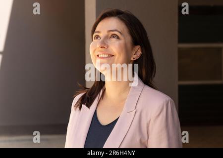 Portrait Happy Mature 40 Yo Beautiful Woman lächelnd mit Zähnen. Kaukasische Burnette Weiblich Mit Braunen Augen Sieht Nach Oben, Trägt Eine Rosafarbene Jacke, Blaues Hemd Stockfoto