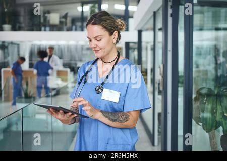 Technologie hilft mir, meine Patientenakten einfach zu organisieren. Eine attraktive junge Krankenschwester im Stehen und mit einem digitalen Tablet in der Klinik. Stockfoto