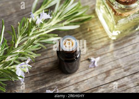 Vervollständigung einer dunklen Flasche ätherischen Öls mit frischen Rosmarin-Zweigen und Blumen Stockfoto