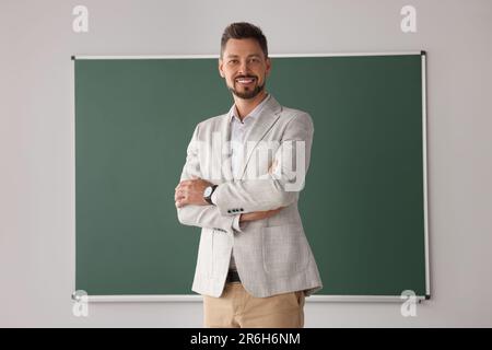 Glückliche Lehrerin, die an der Tafel im Klassenzimmer steht Stockfoto