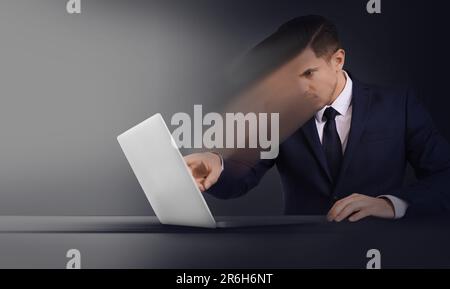 Gedankenkontrolle, Gehirnwäsche oder Zwangskonzepte bei der Arbeit. Ein Mann, der sich am Tisch in einem Laptop auflöst Stockfoto