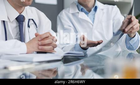 Zwei Ärzte schauen sich Röntgenbilder an und besprechen die Diagnose. Sie sitzen 1 Stockfoto