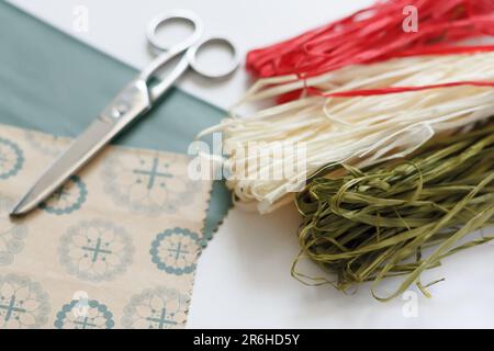 Handwerkliche Verpackungen. Dekoratives Verpackungspapier, Scheren und Sträucher aus natürlichem Seil in Rot, Weiß und Grün auf weißem Hintergrund Stockfoto