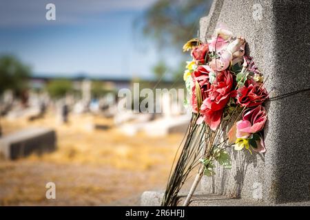 Künstliche Blumen, zerschmettert von der Hitze und Sonne, auf einem Grabstein auf dem Concordia Friedhof in El Paso, Texas. Stockfoto