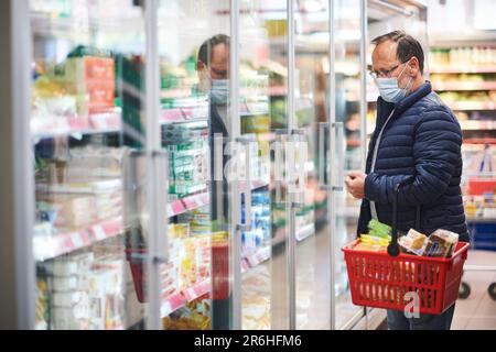 Mann mittleren Alters, der Lebensmittel im Supermarkt kauft, trägt medizinische Maske Stockfoto