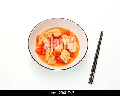 Ein Overhead Shot eines traditionellen asiatischen Hühnereintopfs, serviert in einer weißen Schüssel mit Stäbchen auf einem weißen Tisch Stockfoto