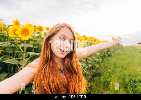 Außenporträt eines süßen jungen rothaarigen Mädchens, das sich auf dem Sonnenblumenfeld posiert Stockfoto