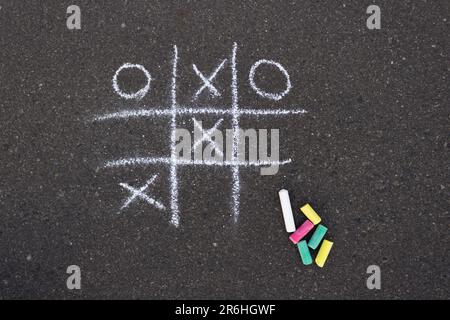 Mit weißer Kreide auf dem Bürgersteig gemalt. TIC-tac-Toe-Spiel. Neben dem Bild befinden sich farbige Kreideteile. Stockfoto