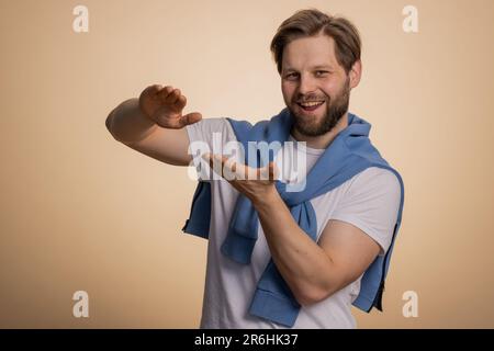 Ein junger Kaukasier, der Geld verschwendet, mehr Trinkgelder, großen Gewinn, Lotterie-Jackpot gewinnt, Erfolgreicher Einkauf, Bezahlung, Cashback. Ein Typ isoliert auf beigefarbenem Studiohintergrund Stockfoto