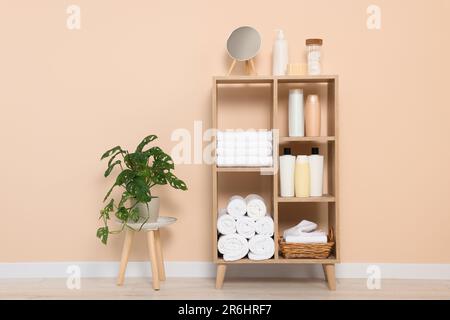Weiche gefaltete Handtücher und Kosmetikflaschen auf Holzregalen nahe beigefarbener Wand Stockfoto