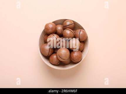 Köstliche Bio-Macadamia-Nüsse in Holzschüssel auf beigefarbenem Hintergrund, Draufsicht Stockfoto