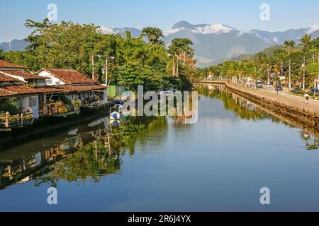 Blick auf den Fluss Perequê-Azu mit Häusern, Vegetation und Regenwaldbergen im Hintergrund an einem sonnigen Tag, Reflexionen über das Wasser in der UNESCO-Welt Heri Stockfoto