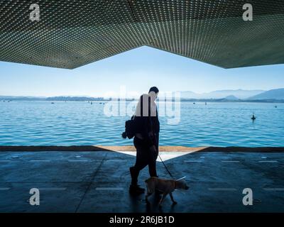 Silhouetten von Menschen, die entlang eines Kais im Hafen von Santander spazieren. Stockfoto