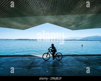 Silhouetten von Menschen, die entlang eines Kais im Hafen von Santander spazieren. Stockfoto