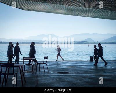 Silhouetten von Menschen, die entlang eines Kais im Hafen von Santander spazieren. Stockfoto