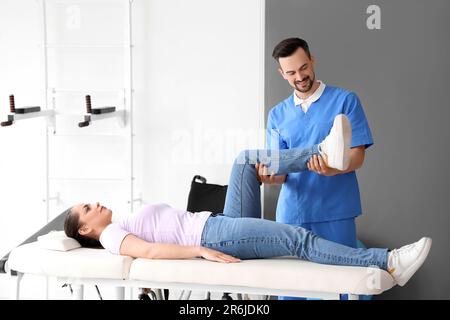 Männlicher Physiotherapeut, der mit einer jungen Frau auf der Couch im Rehabilitationszentrum arbeitet Stockfoto